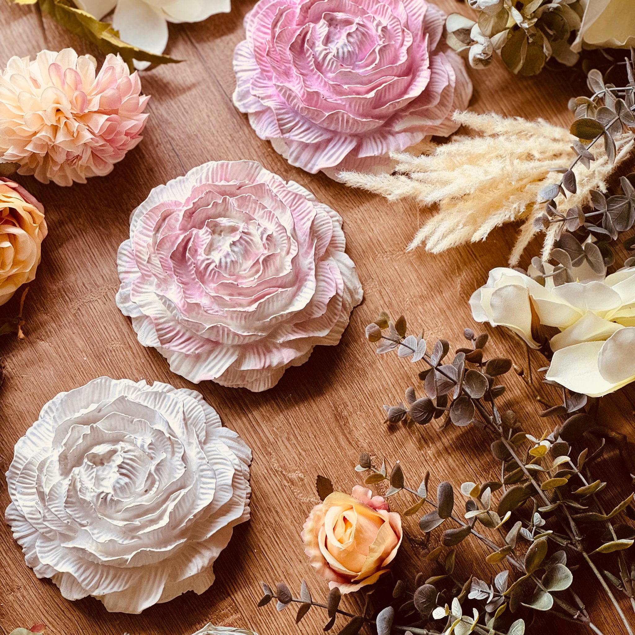 Zart gestaltete Rosenblüten aus Gießkeramik in Rosa, Pink und Creme, dekorativ mit getrockneten Blumen arrangiert, ideale Geschenkidee für Liebhaber floraler Dekoration